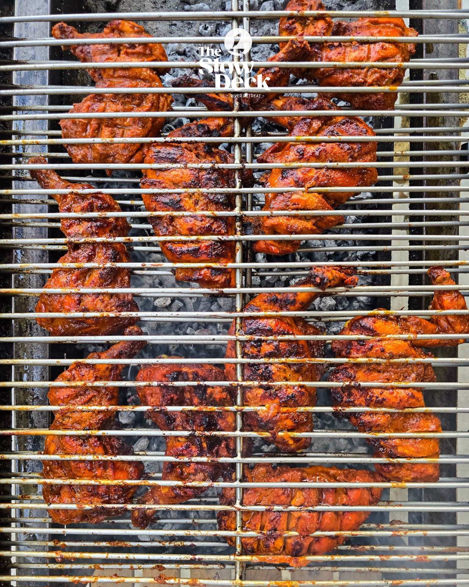 Marinated chicken grilling over charcoal at the Slow Deck River Retreat.